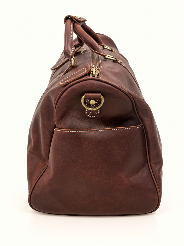 Side view of the Dusty Duffel brown leather weekender bag highlighting the exterior slip pocket, antique brass D-ring, contrast stitching, and zipper details.
