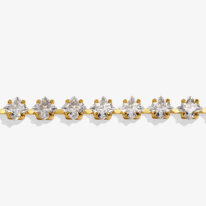 close up of a gold tennis bracelet with clear  floral inspired gemstones on a white background