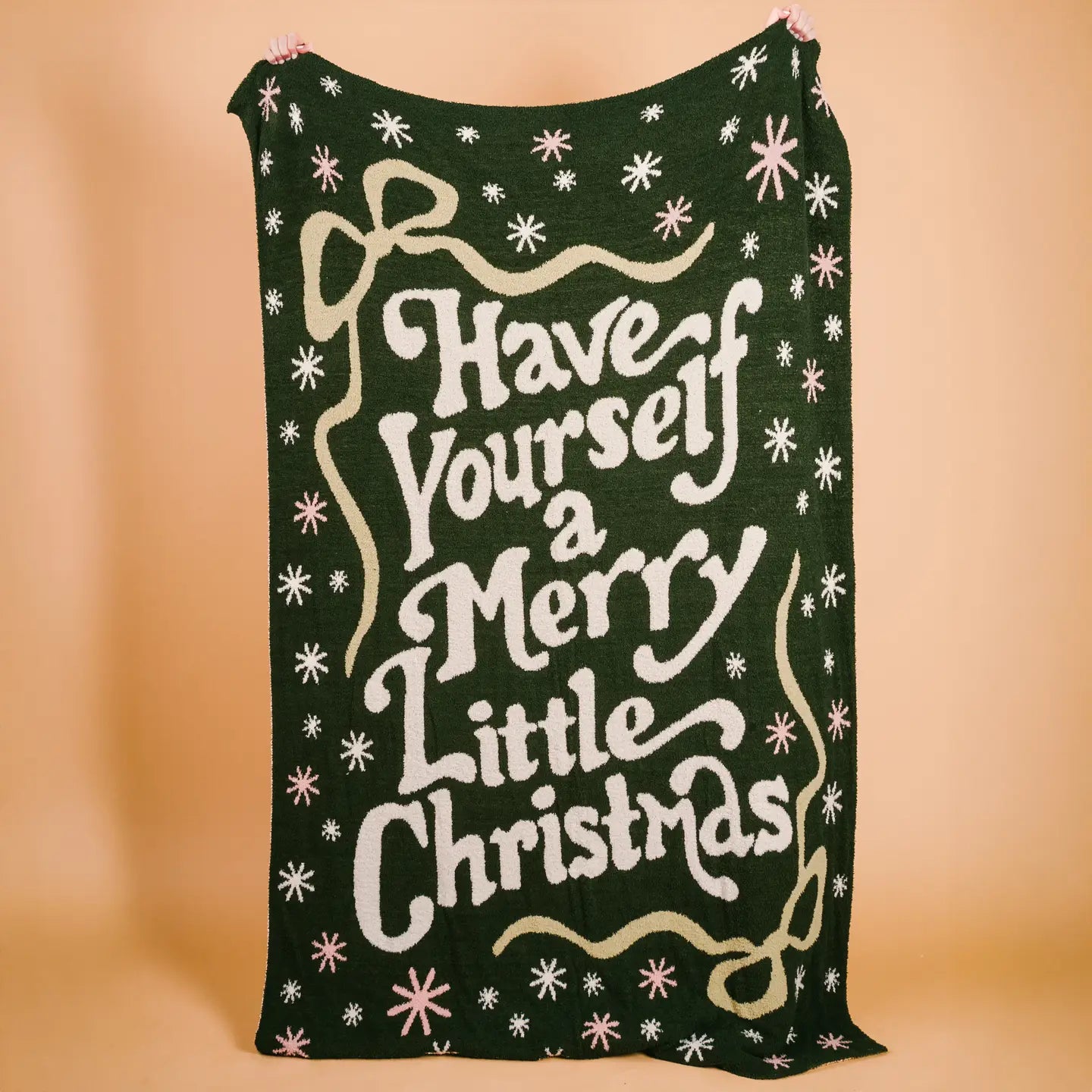 Green knitted blanket with 'Have Yourself a Merry Little Christmas' text on a beige background
