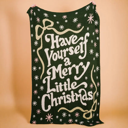 Green knitted blanket with 'Have Yourself a Merry Little Christmas' text on a beige background