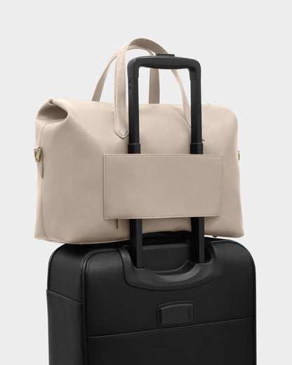 Katie Loxton Milan Cabin Bag in Oyster attached to rolling suitcase handle with built-in luggage sleeve for travel convenience.