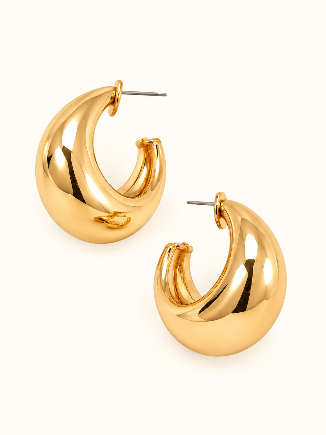 Bold sculpted gold hoop earrings featuring a chunky crescent-shaped design, polished gold-tone finish, and post closures on a cream background.